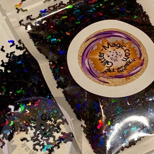 May include: A clear plastic bag filled with black iridescent glitter shaped like bats. The bag has a white label with the text "Glitter Magic" and "Make your own magic".