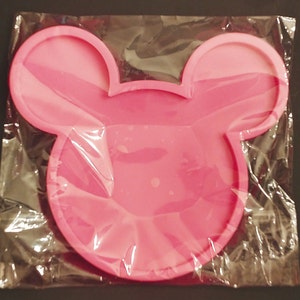 May include: Pink silicone mold shaped like a Mickey Mouse head. The mold is in a clear plastic bag.