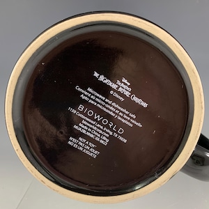 K&ouml;nnte beinhalten: Schwarze Keramiktasse mit breitem Boden und Henkel. Der Boden der Tasse zeigt Text, darunter "The Nightmare Before Christmas" und "BIOWORLD". Die Tasse ist mikrowellen- und sp&uuml;lmaschinenfest.