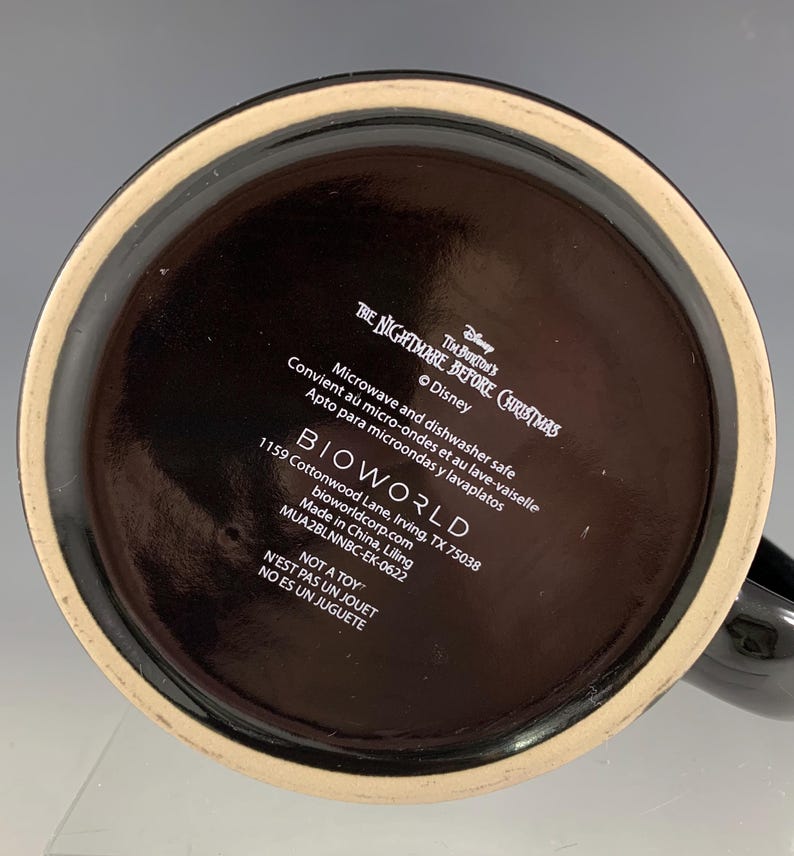 K&ouml;nnte beinhalten: Schwarze Keramiktasse mit breitem Boden und Henkel. Der Boden der Tasse zeigt Text, darunter "The Nightmare Before Christmas" und "BIOWORLD". Die Tasse ist mikrowellen- und sp&uuml;lmaschinenfest.