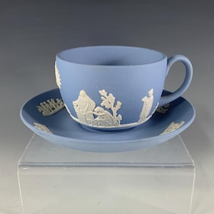 May include: A light blue teacup and saucer set. The cup and saucer are decorated with white relief designs. The cup has a handle and the saucer is round. The set is made of ceramic.