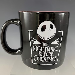 K&ouml;nnte beinhalten: Schwarze Keramik-Tasse mit der Figur Jack Skellington aus "The Nightmare Before Christmas". Die Tasse hat eine wei&szlig;e Grafik von Jacks Gesicht und dem Filmtitel. Der Innenrand ist rosa.