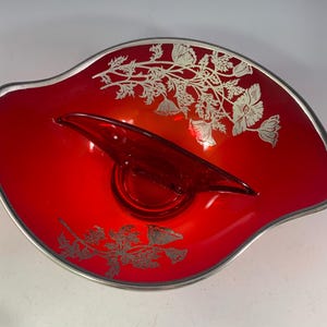 May include: A red glass serving dish with a silver floral design and a small, separate red glass bowl. The dish has a wavy edge and a silver rim.