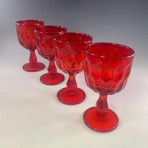 May include: Four red vintage wine glasses. Each glass features a textured pattern on the bowl and a stem with a round base. The glasses are arranged in a diagonal line, showcasing their design and color.