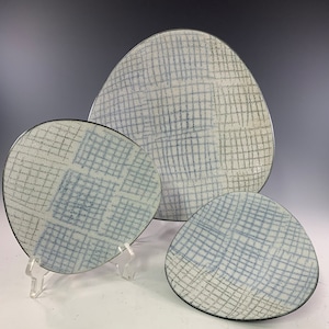 May include: Three ceramic plates in different sizes with a white background and a blue and gray grid pattern.