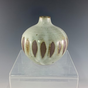 May include: A small, white ceramic vase with a brown and white geometric pattern. The vase has a round body and a narrow neck.
