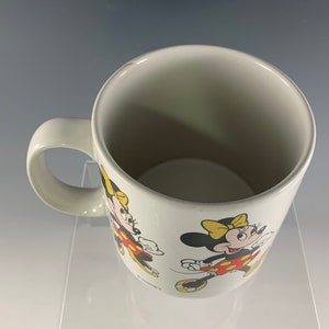 Puede incluir: Taza de cer&aacute;mica blanca con una imagen roja y amarilla de Minnie Mouse. La taza tiene un asa y la imagen de Minnie Mouse se repite en la taza.