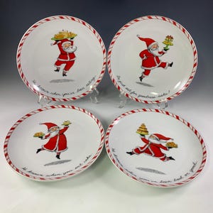May include: Set of four white ceramic Christmas plates with red and white candy cane trim. Each plate features a cartoon Santa Claus carrying a plate of cookies and a festive message. The messages are: "He knows when you've been eating", "So just eat for goodness sake", "He knows when you eat cake", and "He knows when you've been bad or good."