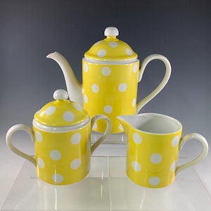 May include: A yellow and white polka dot tea set. The set includes a teapot with a lid, a sugar bowl with a lid, and a creamer. The teapot has a curved spout and handle. The sugar bowl has two handles. The creamer has a handle and a spout.