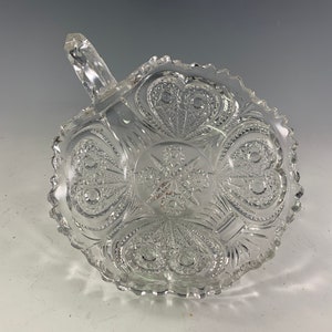 May include: A clear glass bowl with a handle. The bowl has a scalloped edge and a decorative pattern of hearts and stars.