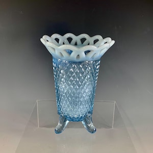 May include: A vintage blue glass vase with a diamond pattern and three small feet. The top rim features a white, openwork design. This decorative vase is a unique piece for home decor.