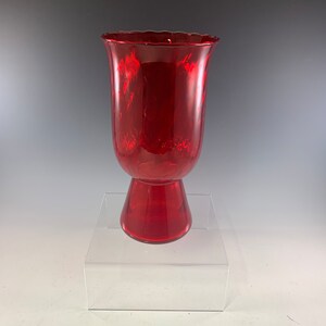 May include: A red glass vase with a flared top and a wide base. The vase has a textured, rippled surface.