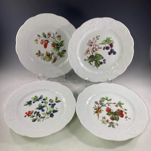 May include: Set of four white ceramic dinner plates with a raised rim and a scalloped edge. Each plate features a different floral design with berries and leaves in shades of red, green, blue, and pink.