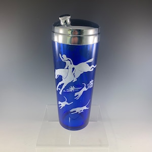 May include: Cobalt blue glass cocktail shaker with a silver top. The shaker has a white etched design of a person riding a horse and several dogs running.