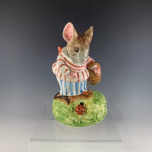 May include: A ceramic figurine of a mouse wearing red and blue striped pajamas, holding a basket and standing on a green base with a ladybug.
