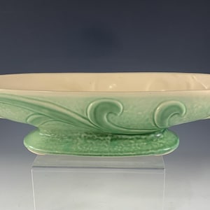 May include: A ceramic centerpiece bowl with a light green exterior and a cream-colored interior. The bowl features a textured base and decorative scrollwork. The handles are curved. The bowl is approximately 14 inches long.
