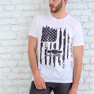 Puede incluir: Camiseta blanca con un diseño de bandera estadounidense desgastado y la palabra "Chevrolet" impresa en negro.