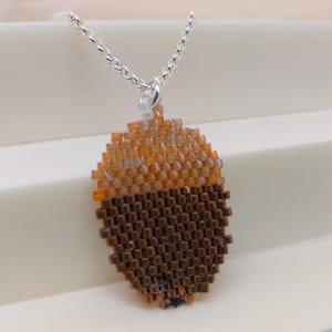 May include: A silver chain necklace with a brown and orange beaded acorn pendant.