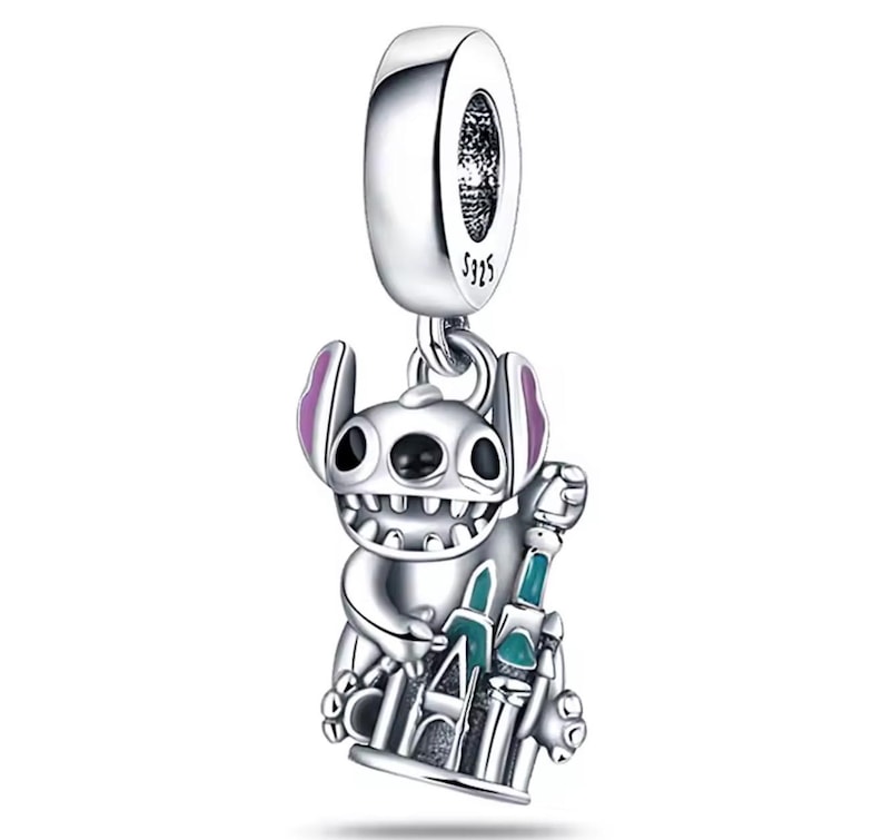 May include: A silver charm featuring a cartoon character with large ears and a wide grin, holding a castle. The charm has purple accents on the ears and a turquoise and green castle. The charm is marked with "S925".
