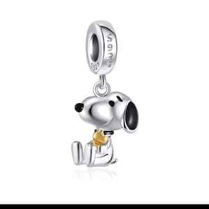 May include: A silver Snoopy charm with a gold star on his chest. The charm is suspended from a silver loop with the word "S925" engraved. A cute and collectible charm for charm bracelets or necklaces.