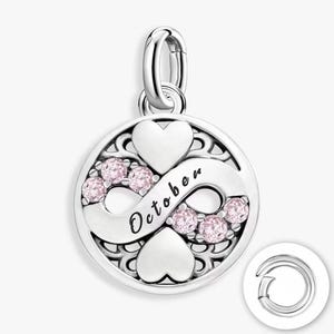 May include: A circular silver charm featuring an infinity symbol intertwined with two hearts. The charm includes the word October in script font and six small, round, light pink stones set along the infinity loop. A silver jump ring is attached.