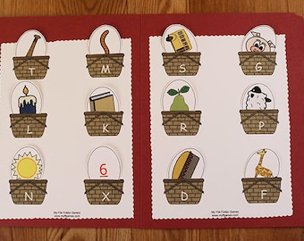 May include: A red folder with a white interior. The folder has a scalloped edge and is divided into two sections. Each section has nine baskets with different objects inside. The objects include a baseball bat, a worm, a school bus, a pig, a candle, a book, a pear, a sheep, a sun, a number six, a loaf of bread, and a giraffe. Each basket has a letter on it.