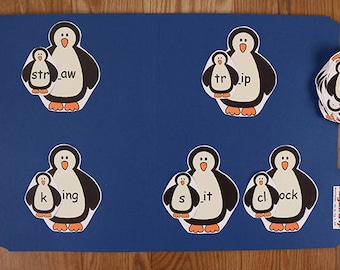May include: A blue file folder featuring penguin-shaped flashcards. Each penguin displays a word segment, like "str_aw" or "tr_ip". A stack of extra penguin cards with "cl" is also visible. The words are likely for phonics practice.