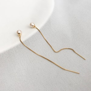May include: A pair of gold chain earrings with small pearl accents. The earrings are delicate and dangle from the earlobe.