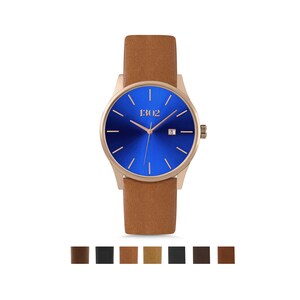 K&ouml;nnte beinhalten: Eine ros&eacute;goldene Uhr mit blauem Zifferblatt und braunem Lederarmband. Das Zifferblatt der Uhr hat ein Datumsfenster und den Markennamen "1302" aufgedruckt.