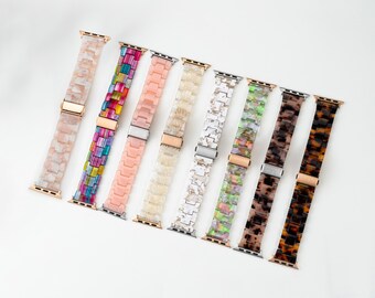 Puede incluir: Ocho correas de reloj dispuestas en fila, con varios diseños de eslabones de resina que incluyen rosa sólido, rayas multicolores y patrones jaspeados en blanco, beige, gris, verde y marrón, cada una con un conector y cierre de metal.