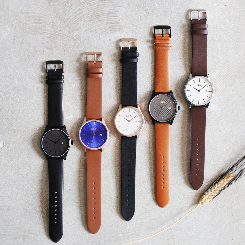 Pode incluir: Cinco rel&oacute;gios de pulso com diferentes cores de pulseiras e designs de mostrador. Os rel&oacute;gios t&ecirc;m pulseiras pretas, castanhas e brancas. Os mostradores s&atilde;o brancos, pretos e azuis.