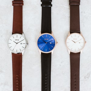 K&ouml;nnte beinhalten: Drei Armbanduhren mit verschiedenen Zifferbl&auml;ttern: wei&szlig;, blau und cremefarben. Jede Uhr hat ein Lederarmband in einer anderen Farbe: braun, schwarz und dunkelbraun. Die Uhren tragen alle den gleichen Markennamen "D102" auf dem Zifferblatt.