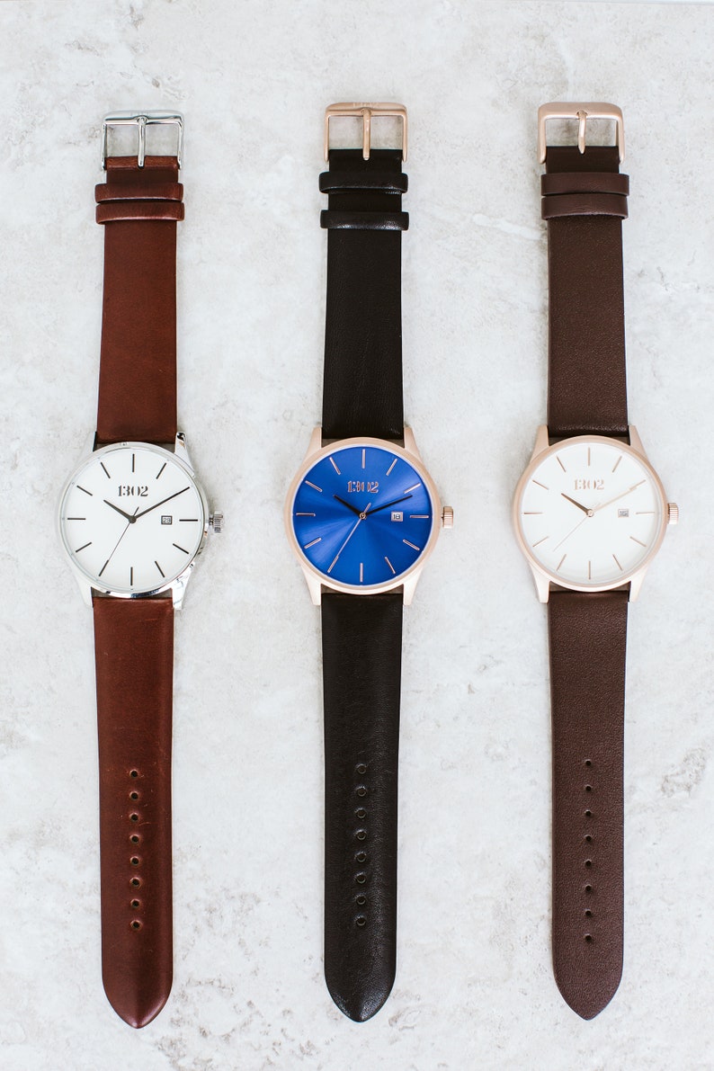 K&ouml;nnte beinhalten: Drei Armbanduhren mit verschiedenen Zifferbl&auml;ttern: wei&szlig;, blau und cremefarben. Jede Uhr hat ein Lederarmband in einer anderen Farbe: braun, schwarz und dunkelbraun. Die Uhren tragen alle den gleichen Markennamen "D102" auf dem Zifferblatt.