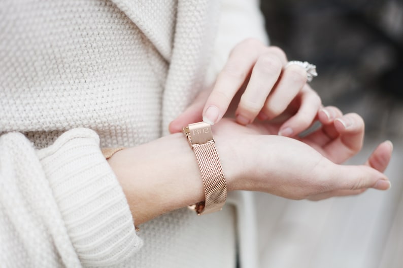 May include: A rose gold metal watch band with a mesh design. The band has a clasp with the number "1302" engraved on it.