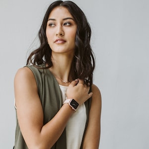 Puede incluir: Una mujer con un chaleco verde sin mangas sobre una camisa blanca y un Apple Watch de oro rosa con una banda marr&oacute;n claro.