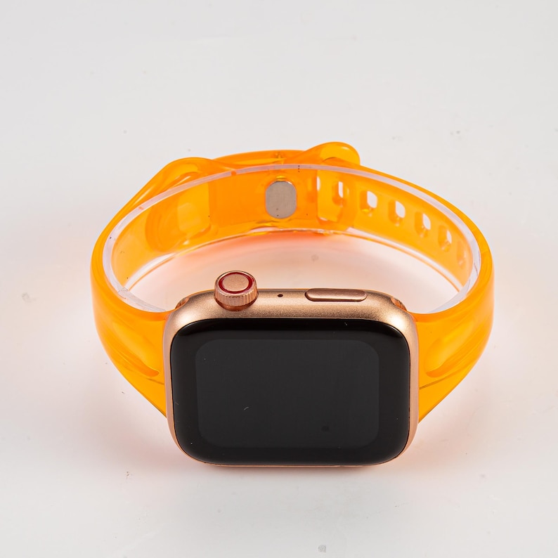 K&ouml;nnte beinhalten: Eine goldene Apple Watch mit einem leuchtend orangefarbenen, durchsichtigen Silikonarmband. Das Zifferblatt der Uhr ist schwarz und das Armband hat einen magnetischen Verschluss.