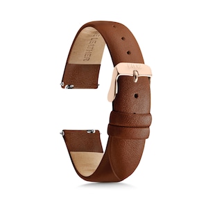 May include: A brown leather watch strap with a rose gold-toned metal buckle and two matching leather loops. The inner side of the strap is light tan and features the embossed text "GENUINE LEATHER". It includes silver-toned spring bar pins.