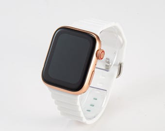 Könnte beinhalten: Eine weiße Apple Watch mit einem roségoldenen Armband und einem schwarzen Bildschirm. Die Uhr steht auf einem weißen Ständer.