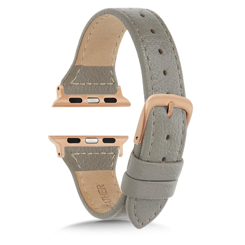 May include: A grey leather watch strap with rose gold connectors and a buckle. The strap is made of textured leather and has a light beige interior. The rose gold connectors are for a smartwatch.