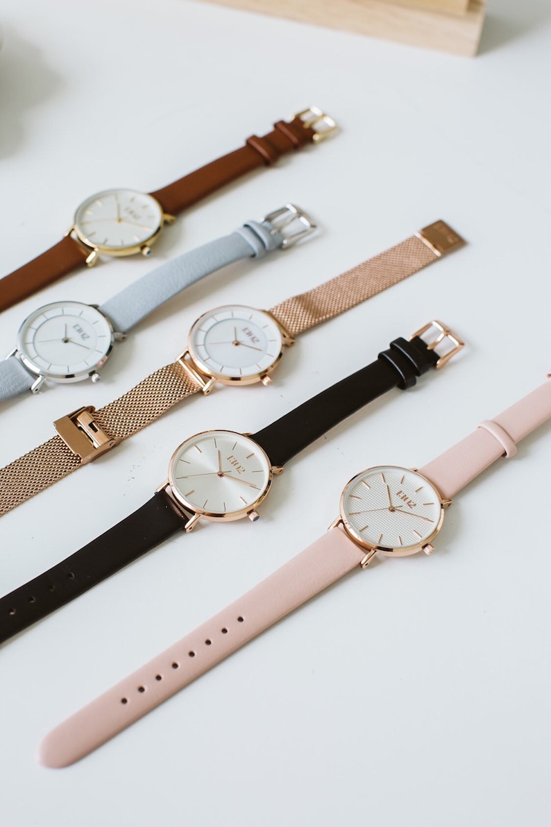 Puede incluir: Cinco relojes de pulsera con correas de diferentes colores y esferas blancas. Las correas son de cuero marr&oacute;n, cuero azul claro, malla dorada, cuero negro y cuero rosa. Las esferas de los relojes tienen todas la palabra "TIME" impresa en ellas.