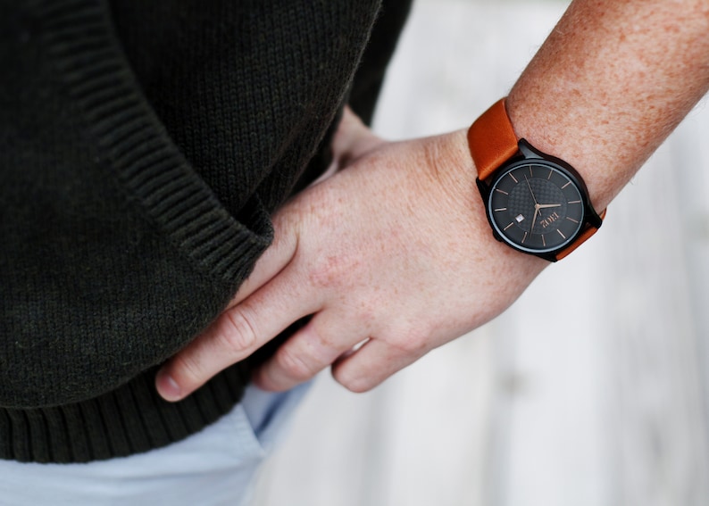 Pode incluir: Um rel&oacute;gio de pulso preto com uma pulseira de couro marrom. O mostrador do rel&oacute;gio tem um fundo preto com marcas brancas e a palavra "TIME" em letras brancas.