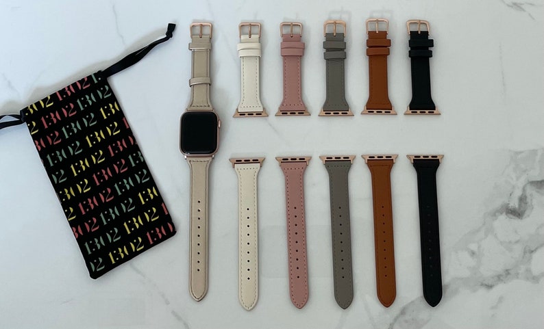 May include: An Apple Watch with a light beige leather strap and rose gold hardware, with a selection of interchangeable straps in various colours. A black drawstring bag with the text "1302" in multiple colours is also present.