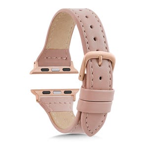 May include: A pale pink leather watch strap with rose gold-coloured connectors and a buckle. The strap has a smooth finish and a traditional buckle. The connectors are designed for a smartwatch.