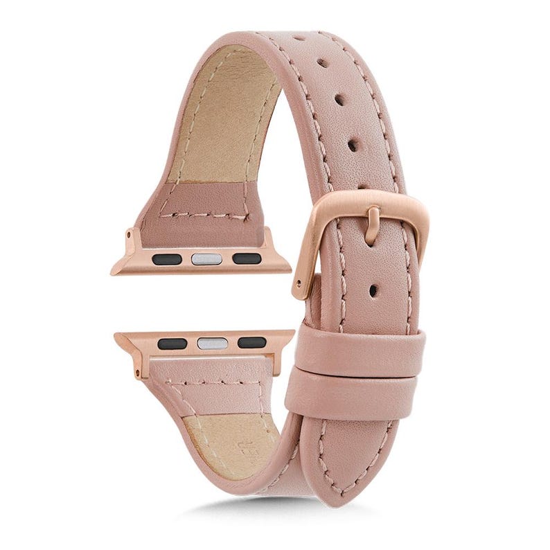 May include: A pale pink leather watch strap with rose gold-coloured connectors and a buckle. The strap has a smooth finish and a traditional buckle. The connectors are designed for a smartwatch.