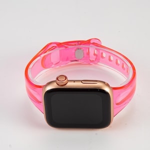 K&ouml;nnte beinhalten: Ein durchsichtiges rosa Silikon-Armband f&uuml;r eine Apple Watch. Das Armband ist durchsichtig und hat ein goldenes Zifferblatt.