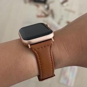May include: A rose gold Apple Watch with a brown leather band.