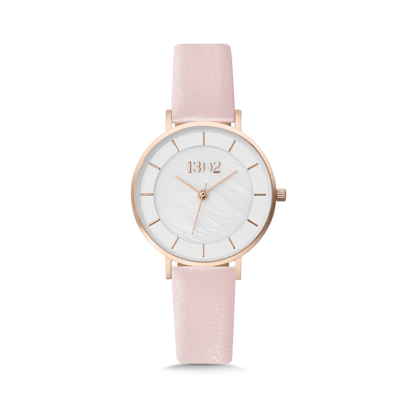 May include: A rose gold watch with a white face and a pink leather band. The watch face has a mother-of-pearl effect and the brand name "1302" is printed on the face.