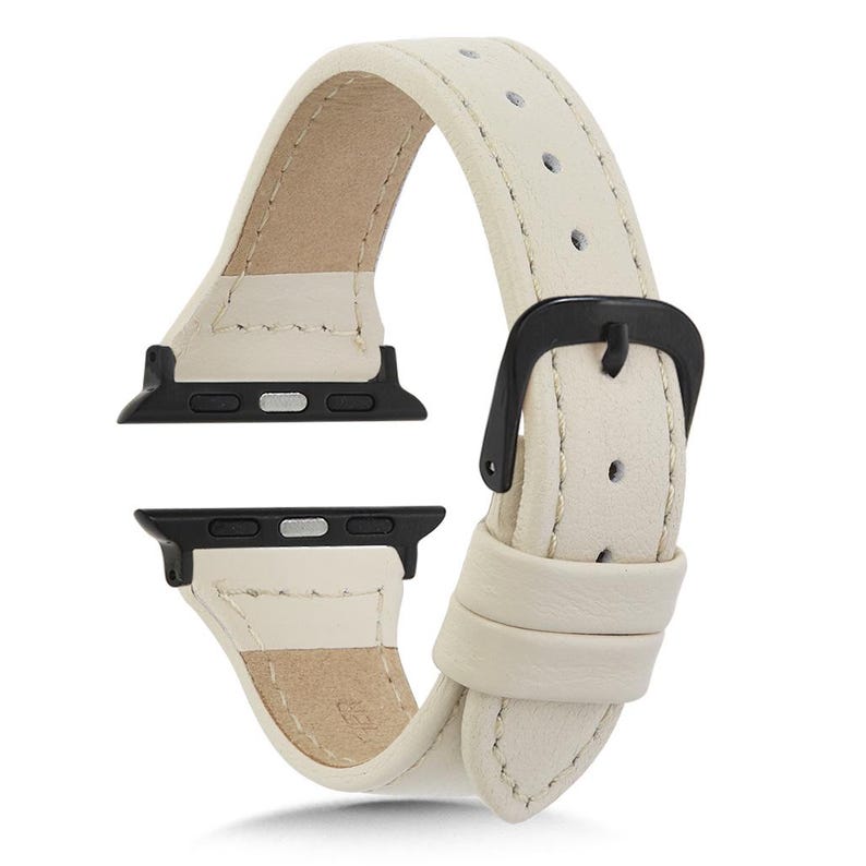 May include: Cream leather watch strap with a black buckle and black connectors. The strap has a smooth, textured finish and a classic design. The strap is designed to fit a smartwatch.