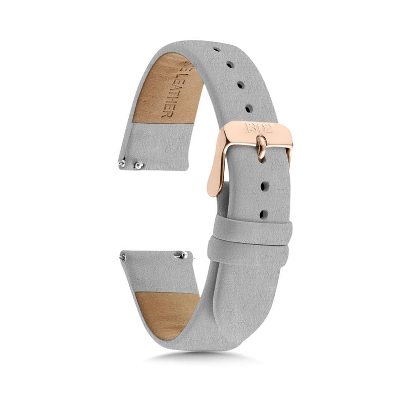 May include: A light gray watch strap made of leather with a rose gold metal buckle. The strap features a series of adjustment holes and two sliding loops. The interior of the strap is stamped with the text GENUINE LEATHER and the buckle is engraved.