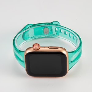 K&ouml;nnte beinhalten: Eine ros&eacute;goldene Apple Watch mit einem durchsichtigen t&uuml;rkisfarbenen Silikonarmband. Das Zifferblatt der Uhr ist schwarz und das Armband hat einen Schlie&szlig;enverschluss.